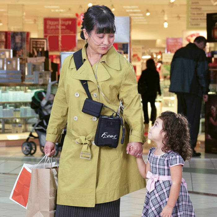 Woman holding the hand of a small girl while wearing nasal cannula attached to an AirSep Focus Portable Oxygen Concentrator