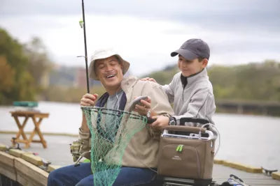 Man wearing nasal cannula attached to Respironics SimplyGo Portable Oxygen Concentrator, laughing with a young boy while holding a fish and a fishing net
