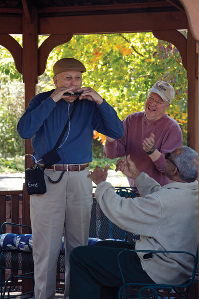 Old man playing the flute and laughing with 2 other friends while wearing a nasal cannula attached to an AirSep Focus Portable Oxygen Concentrator