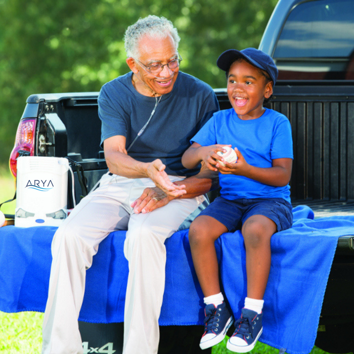 Old man wearing nasal cannula using ARYA Portable Oxygen Concentrator sitting next to a young boy