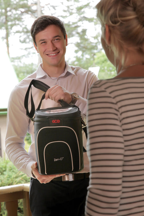 Smiling man holding a GCE Zen-O Portable Oxygen Concentrator that's inside a carry bag to a woman