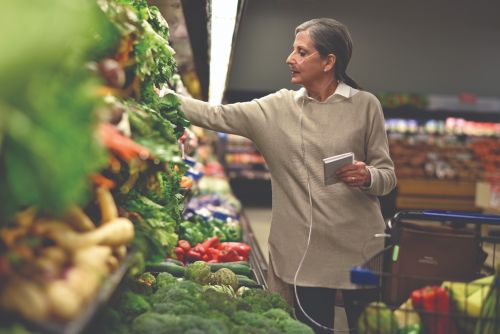 Woman buying vegetables while wearing nasal cannula attached to a Respironics SimplyGo Mini Portable Oxygen Concentrator